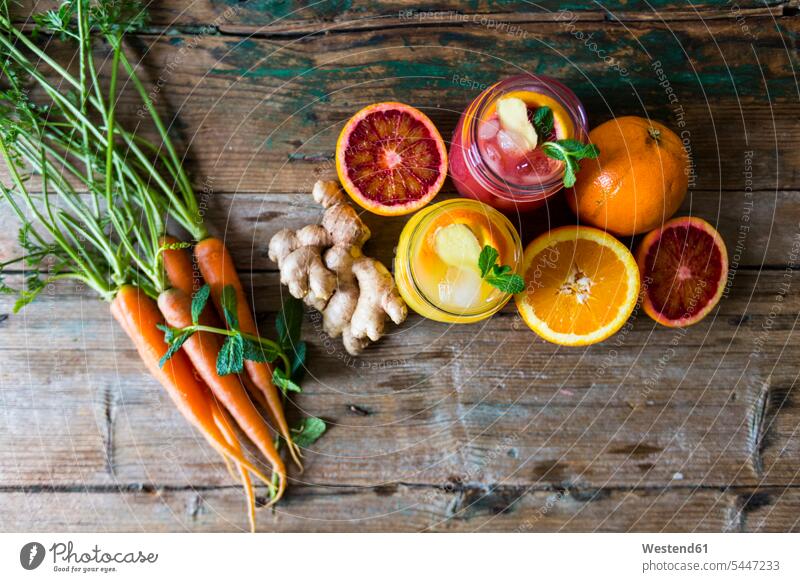 Zwei Gläser mit verschiedenen Orangensäften, Orangen, Karotten, Minzblättern und Ingwer eisgekühlt eisgekuehlt eisgekühlte Pfefferminze fruchtig aufgeschnitten