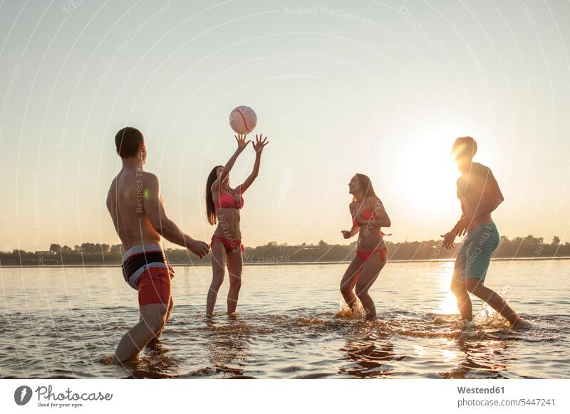 Glückliche Freunde spielen mit einem Ball im Wasser Spaß Spass Späße spassig Spässe spaßig See Seen Freundschaft Kameradschaft Gewässer Volleyball Sonne Abend