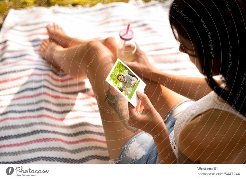 Junge Frau sitzt auf einer Decke und schaut auf ein Sofortbild sitzen sitzend weiblich Frauen Foto Fotos ansehen Erwachsener erwachsen Mensch Menschen Leute