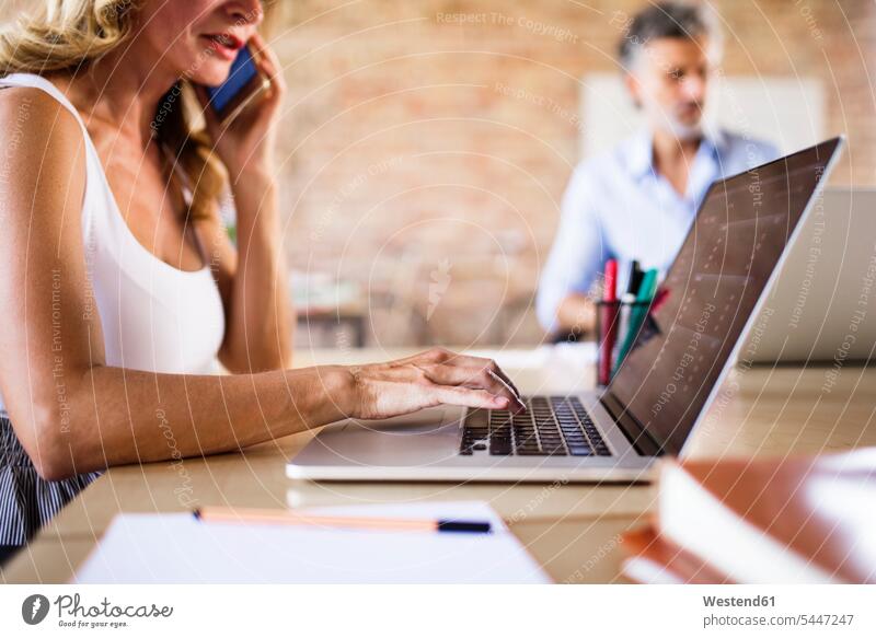 Geschäftsfrau benutzt Handy und Laptop am Schreibtisch im Büro arbeiten Arbeit Office Büros Notebook Laptops Notebooks Arbeitstisch Schreibtische Geschäftsmann