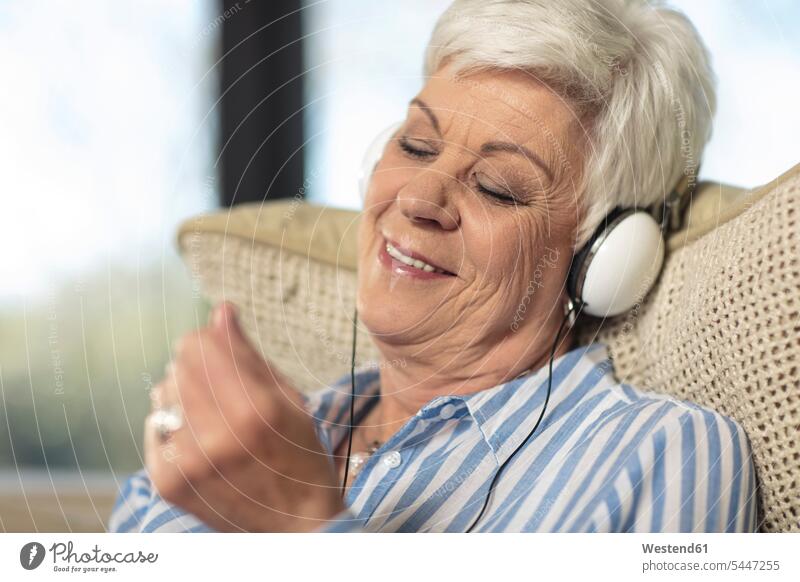 Lächelnde ältere Frau mit Kopfhörern, die zu Hause Musik hört Kopfhoerer Seniorin Seniorinnen alt Zuhause daheim weiblich Frauen lächeln hören hoeren Senioren