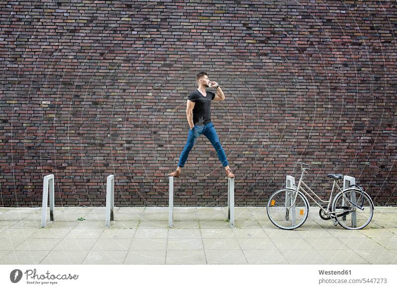 Mann mit Handy balanciert auf Fahrradträger vor Ziegelmauer ernst Ernst Ernsthaftigkeit ernsthaft Ziegelwand Backsteinmauer stehen stehend steht Männer männlich