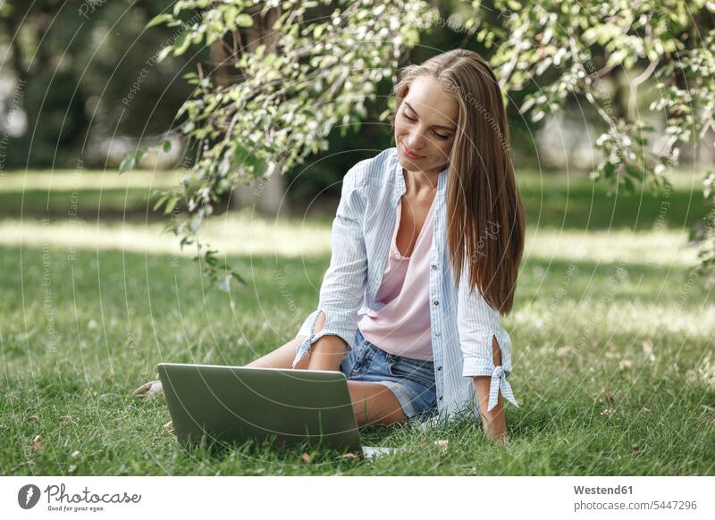 Junge Frau mit Laptop auf einer Wiese lächeln Notebook Laptops Notebooks weiblich Frauen Park Parkanlagen Parks Computer Rechner Erwachsener erwachsen Mensch