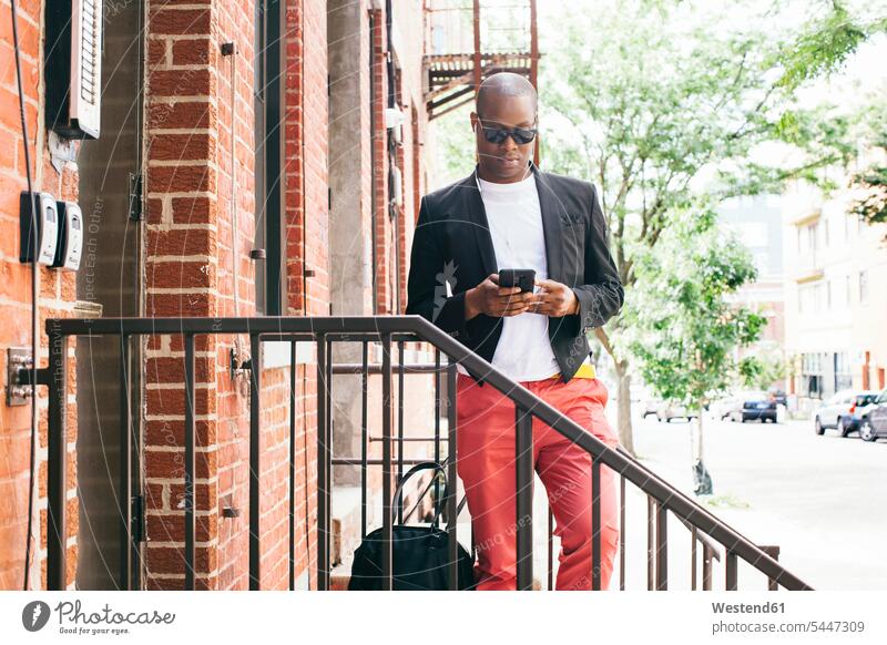 USA, NYC, Brooklyn, Mann wartet auf der Treppe, benutzt Smartphone Männer männlich iPhone Smartphones warten cool Coolness lesen Lektüre hip trendy stehen