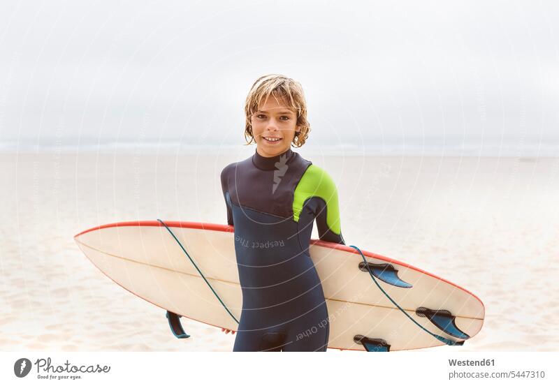 Spanien, Aviles, Porträt eines lächelnden jungen Surfers mit Surfbrett am Strand Meer Meere Teenager Jugendliche Heranwachsende Pubertierende Beach Straende