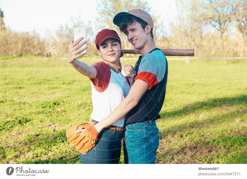 Lächelndes junges Paar mit Baseball-Ausrüstung macht ein Selfie im Park Selfies Handy Mobiltelefon Handies Handys Mobiltelefone lächeln Baseballspiel