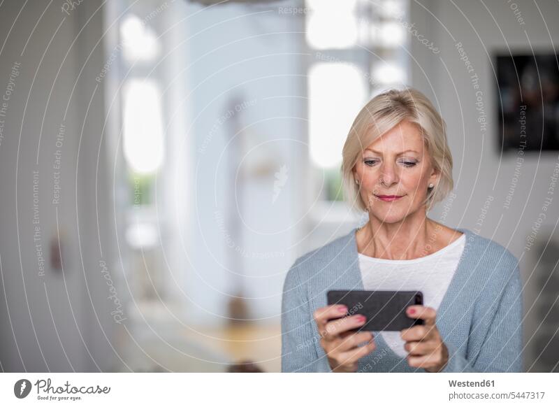 Porträt einer älteren Frau zu Hause, die auf ihr Handy schaut Seniorin Seniorinnen alt Smartphone iPhone Smartphones Portrait Porträts Portraits Senioren