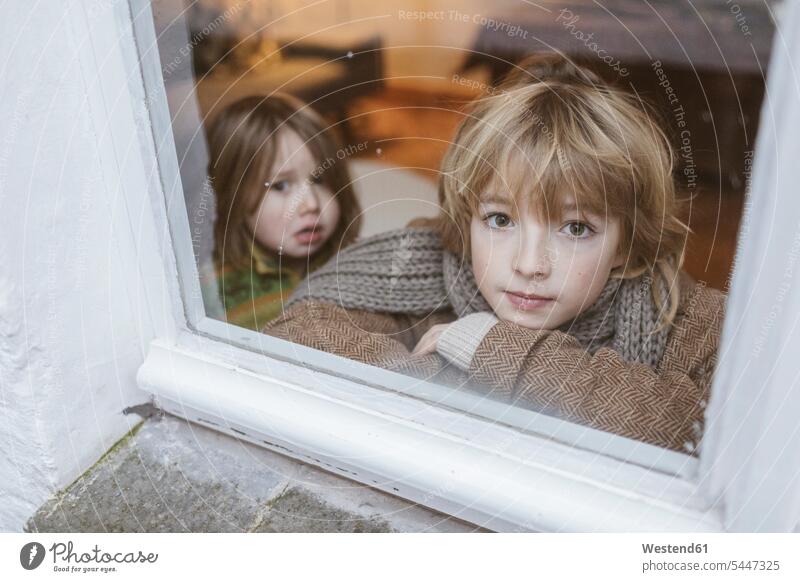 Porträt eines aus dem Fenster blickenden Jungen mit seiner kleinen Schwester im Hintergrund Schwestern schauen schauend anschauen betrachten Geschwister Familie