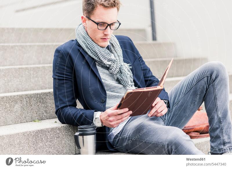 Junger Geschäftsmann sitzt auf einer Treppe und benutzt ein digitales Tablett Urban städtisch Urbanität Urbanitaet Treppenaufgang Tablet Computer Tablet-PC