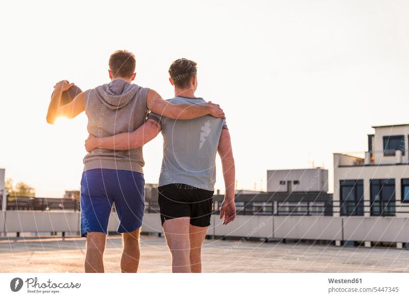 Freunde spielen bei Sonnenuntergang auf einem Dach Basketball jung fit umarmen Sport Freundschaft Team Textfreiraum Vitalität Vertrauen Ball Solidarität