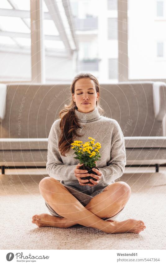 Frau mit geschlossenen Augen sitzt auf dem Boden und hält eine Blume sitzen sitzend Blumen Blüte weiblich Frauen entspannt entspanntheit relaxt Pflanze