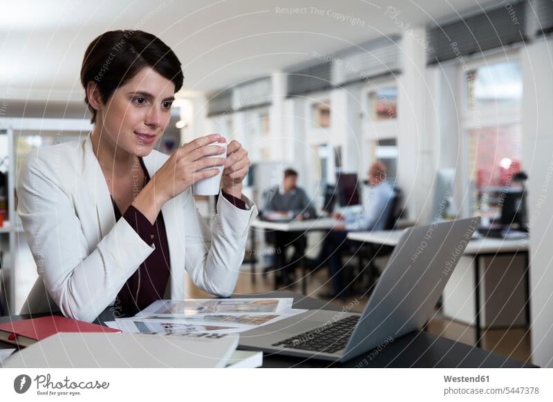 Frau mit Laptop im Büro mit Kollegen im Hintergrund Notebook Laptops Notebooks Geschäftsfrau Geschäftsfrauen Businesswomen Businessfrauen Businesswoman weiblich
