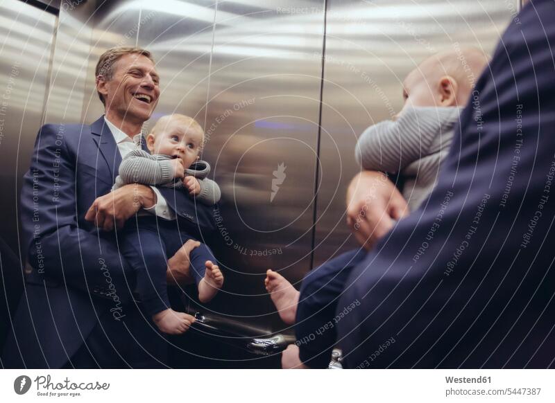 Glücklicher reifer Geschäftsmann hält Baby Boy im Fahrstuhl im Spiegel Businessmann Businessmänner Geschäftsmänner halten Babies Babys Säuglinge Kind Kinder