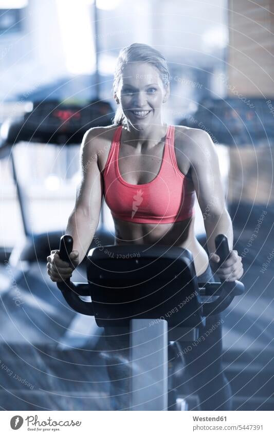 Porträt einer lächelnden Frau auf einem Spinning Bike in der Turnhalle Heimtrainer Hometrainer Trimmräder Trimmrad trainieren weiblich Frauen Fitnessstudio