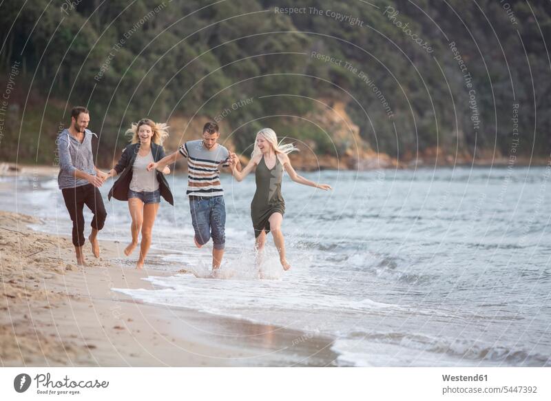 Vier glückliche Freunde laufen am Strand lachen Glück glücklich sein glücklichsein Spaß Spass Späße spassig Spässe spaßig rennen positiv Emotion Gefühl