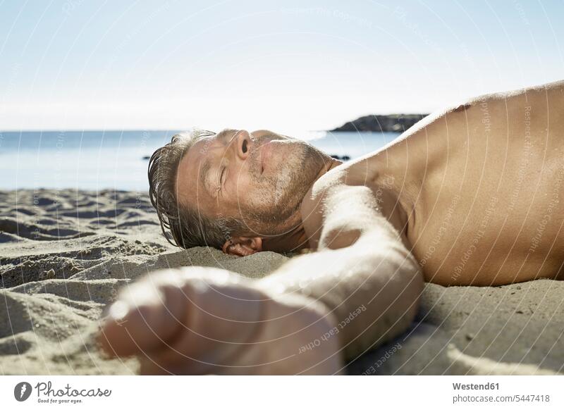Erwachsener Mann entspannt sich am Sandstrand Strand Beach Straende Strände Beaches Männer männlich erwachsen Mensch Menschen Leute People Personen liegen