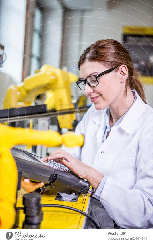 Frau benutzt Gerät in Fabrik mit Industrierobotern Fabriken Ingenieurin Ingenieurinnen Roboter industriell Gewerbe Industrien Männerberuf Business