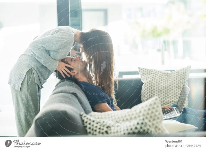 Zu Hause verliebtes junges Paar küssen Küsse Kuss Pärchen Paare Partnerschaft Mensch Menschen Leute People Personen Sofa Couches Liege Sofas Laptop Notebook
