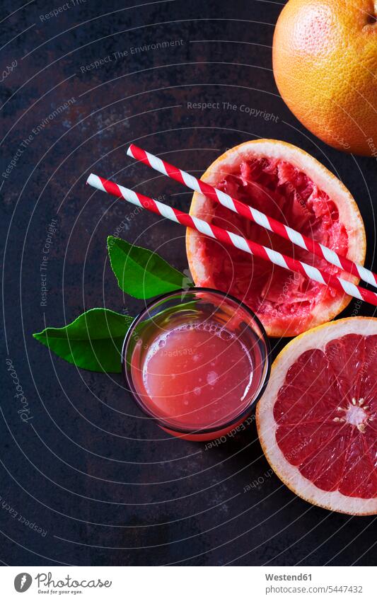 Ganze und in Scheiben geschnittene rosa Grapefruit, Blätter, Strohhalme und Glas Grapefruitsaft Textfreiraum Frucht Früchte Fruechte Gesunde Ernährung