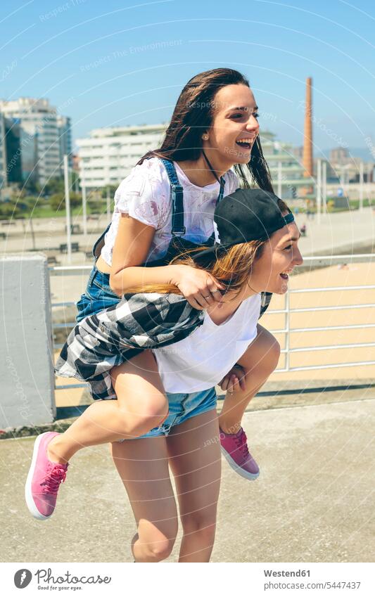 Junge Frau, die ihren Freund huckepack auf der Dachterrasse mitnimmt Huckepack Freundinnen Freunde Freundschaft Kameradschaft lachen weiblich Frauen