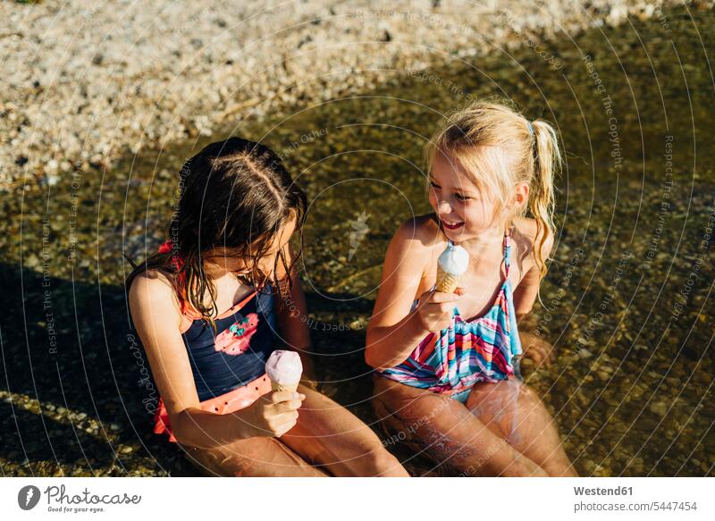 Zwei Mädchen sitzen am Seeufer im Wasser und essen Eiscreme weiblich Freundinnen Speiseeis Kind Kinder Kids Mensch Menschen Leute People Personen Freunde