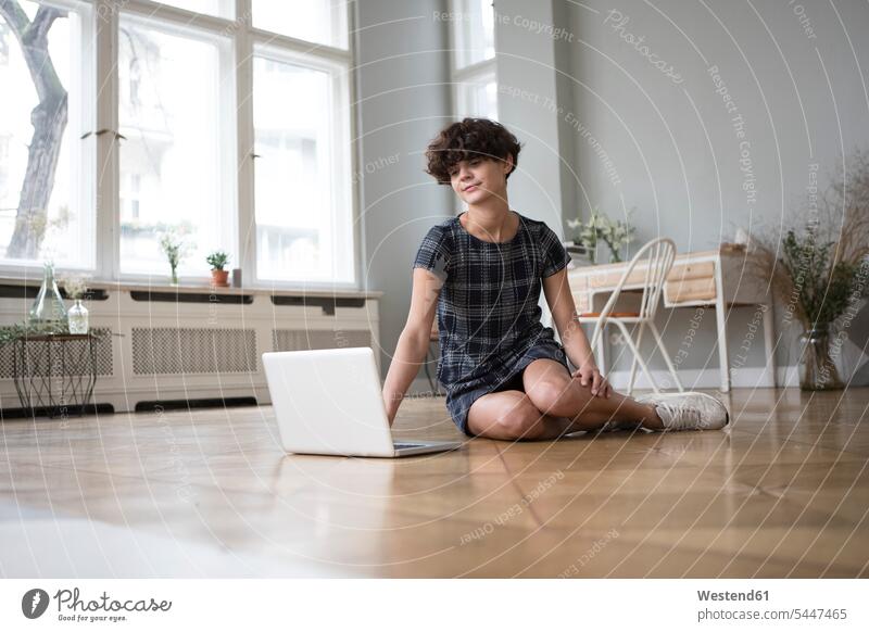 Junge Frau sitzt zu Hause auf dem Boden und schaut auf den Laptop weiblich Frauen Notebook Laptops Notebooks Erwachsener erwachsen Mensch Menschen Leute People