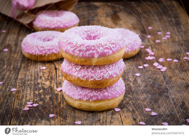Stapel von Doughnuts mit rosa Glasur und Zuckergranulat auf Holz übereinander obenauf aufeinander Zuckerguss Zuckerguß Streudekor süß Süßes rosafarben Streusel