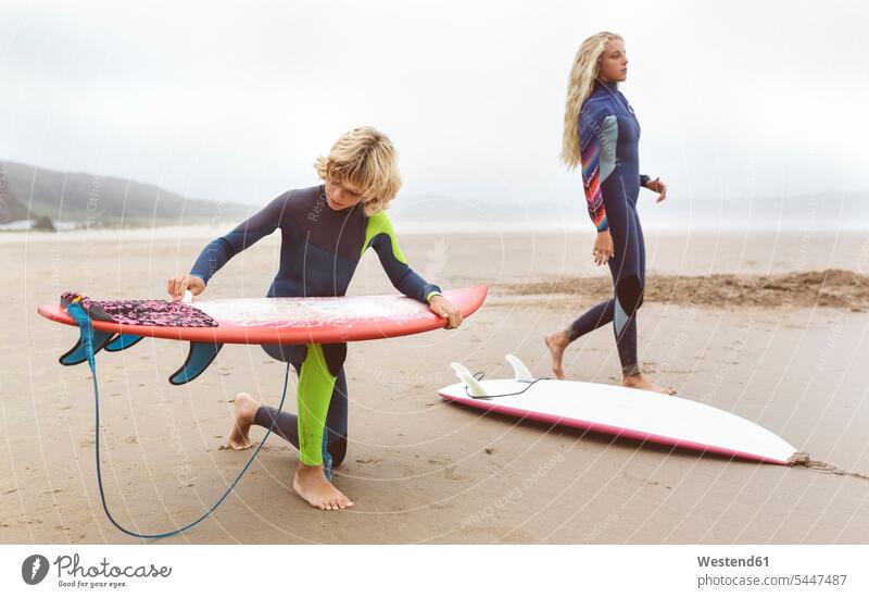 Spanien, Aviles, zwei junge Surfer am Strand bei der Vorbereitung ihrer Surfbretter Beach Straende Strände Beaches Wellenreiter Teenager Jugendliche