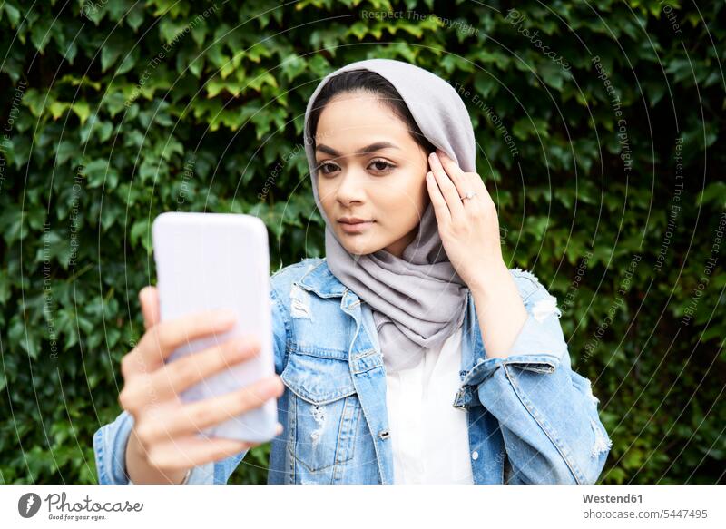 Junge Frau schaut auf ihren Telefonbildschirm und trägt einen Hijab Kopftuch Kopftücher muslimisch Moslem Muslim Handy Mobiltelefon Handies Handys Mobiltelefone