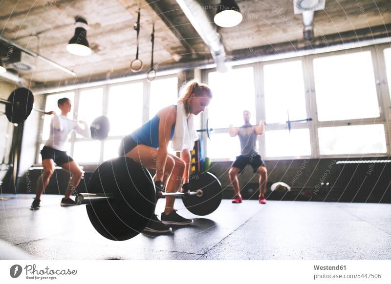 Junge Frau mit Trainingspartnern bereitet sich im Fitnessstudio auf das Hanteltraining vor Gewicht Gewichte trainieren Fitnessgerät Fitnessgeräte Fitnessgeraete
