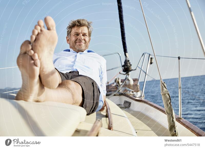 Porträt eines lächelnden, reifen Mannes, der an Deck seines Segelbootes liegt Männer männlich Portrait Porträts Portraits Segeln segelnd segelt Erwachsener