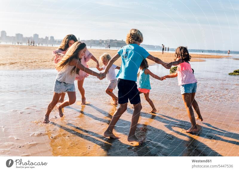 Gruppe von sechs Kindern spielt Ring-a-Ring-a-Rosen am Strand Ringelreihen Beach Straende Strände Beaches Freunde Freundschaft Kameradschaft Gruppe von Menschen