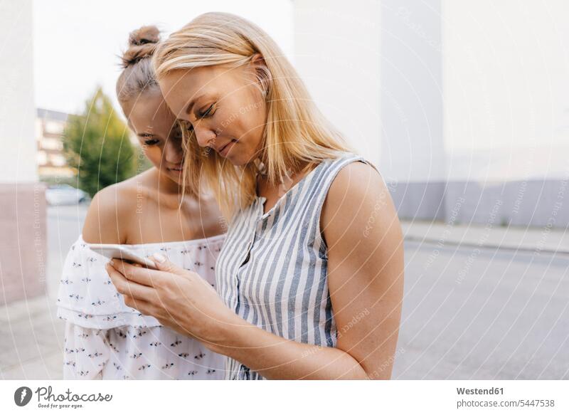 Zwei lächelnde junge Frauen teilen sich ein Mobiltelefon im Freien Freundinnen Handy Handies Handys Mobiltelefone weiblich Teilen Sharing Freunde Freundschaft