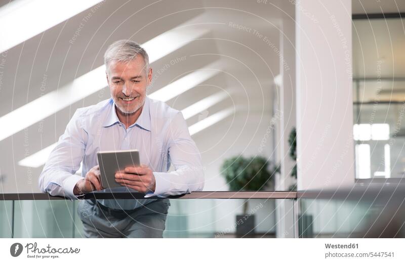 Erfolgreicher Geschäftsmann steht in seinem Büro am Geländer und benutzt digitales Tablett Office Büros Businessmann Businessmänner Geschäftsmänner arbeiten