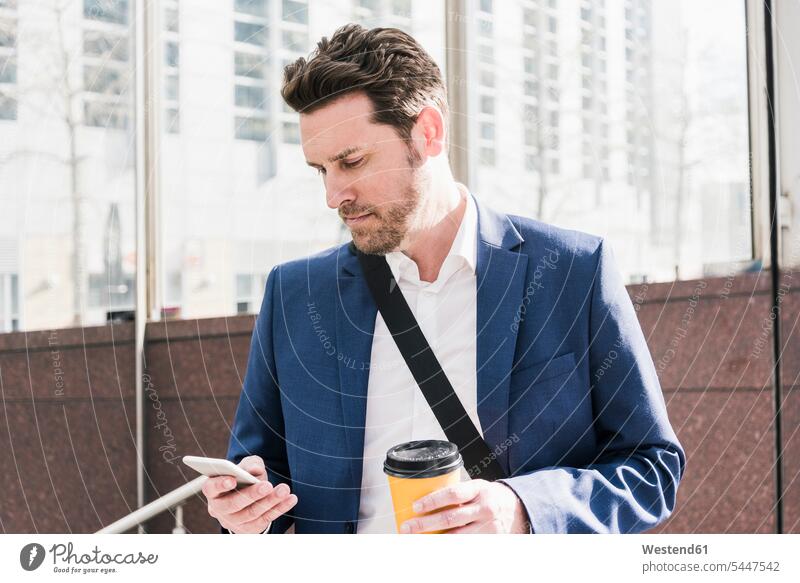Geschäftsmann in der Stadt, liest Smartphone-Nachrichten und hält eine Tasse Kaffee iPhone Smartphones Handy Mobiltelefon Handies Handys Mobiltelefone unterwegs