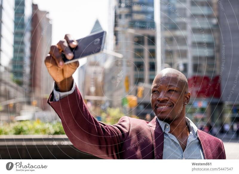 USA, New York City, Manhattan, stilvoller Geschäftsmann macht Selfie mit Smartphone Portrait Porträts Portraits Businessmann Businessmänner Geschäftsmänner