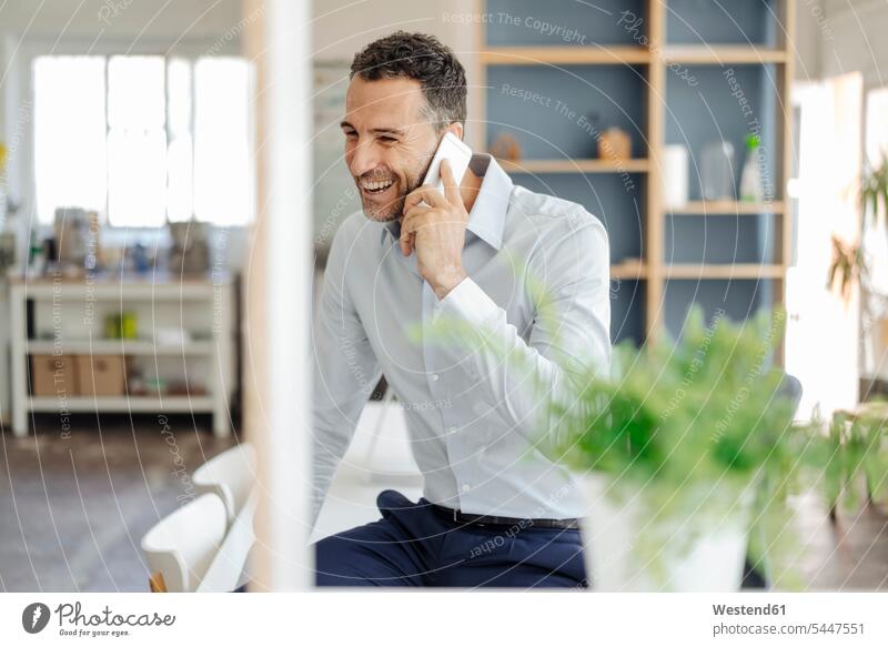 Glücklicher Geschäftsmann im Büro am Handy Mobiltelefon Handies Handys Mobiltelefone lachen Businessmann Businessmänner Geschäftsmänner telefonieren anrufen