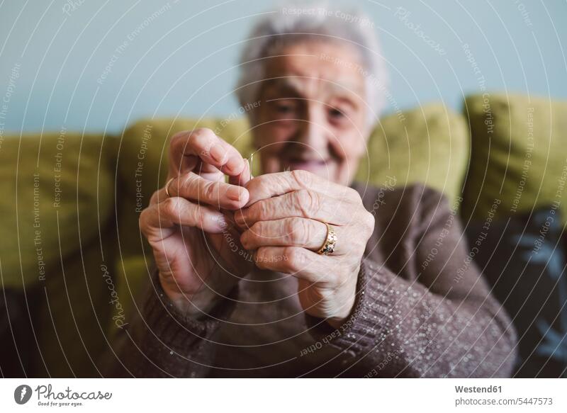 Hände einer älteren Frau, die auf der Couch sitzt und den Faden durch das Knopfloch einer Nähnadel führt einfädeln einfaedeln Faeden Fäden Hand Mensch Menschen