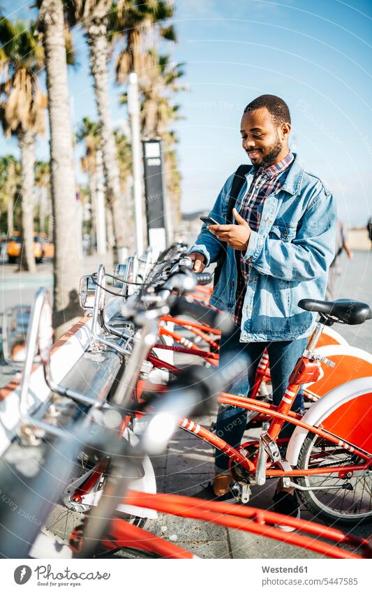 Spanien, Barcelona, junger Mann mit Smartphone, der ein Stadtfahrrad mietet iPhone Smartphones Leihrad Leihräder Männer männlich Handy Mobiltelefon Handies