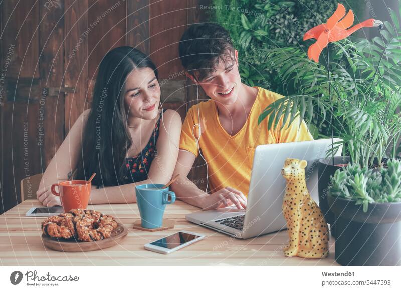 Junges Paar trinkt zu Hause Kaffee und Schokoladenzöpfe mit dem Laptop Notebook Laptops Notebooks Portrait Porträts Portraits Pärchen Paare Partnerschaft