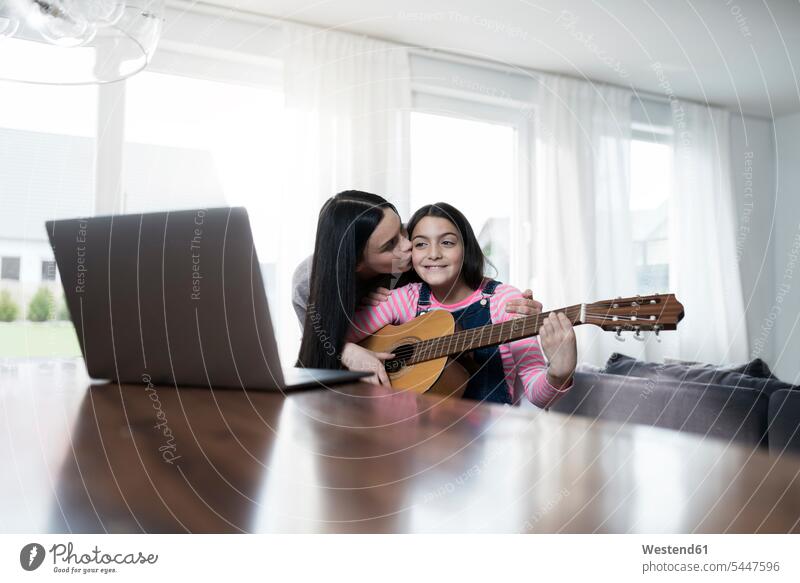 Mutter küsst Tochter, die vor einem Laptop Gitarre spielt Mami Mutti Mütter Mama Töchter Notebook Laptops Notebooks lächeln Gitarren Eltern Familie Familien