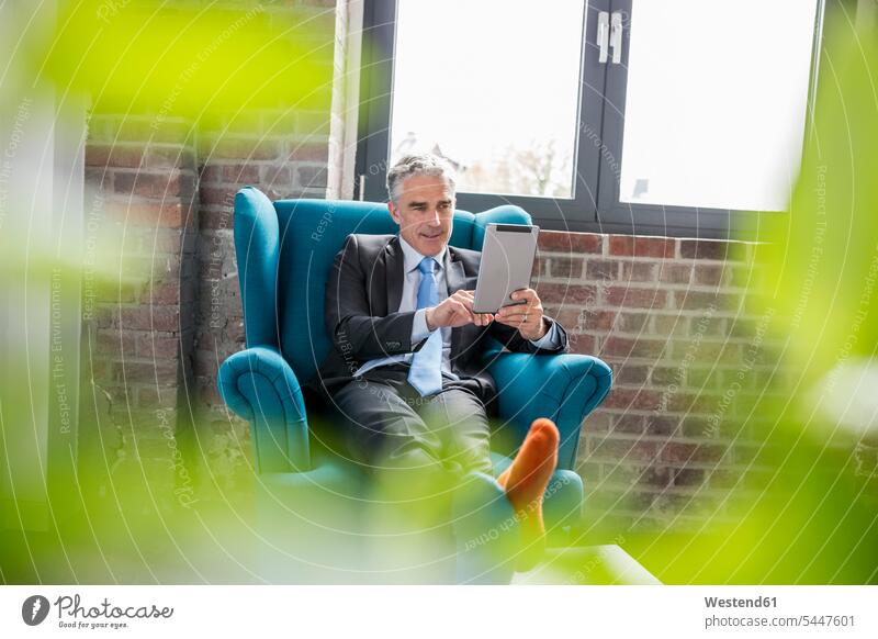 Ein reifer Geschäftsmann sitzt im Sessel und verwendet ein digitales Tablett Businessmann Businessmänner Geschäftsmänner sitzen sitzend arbeiten Arbeit