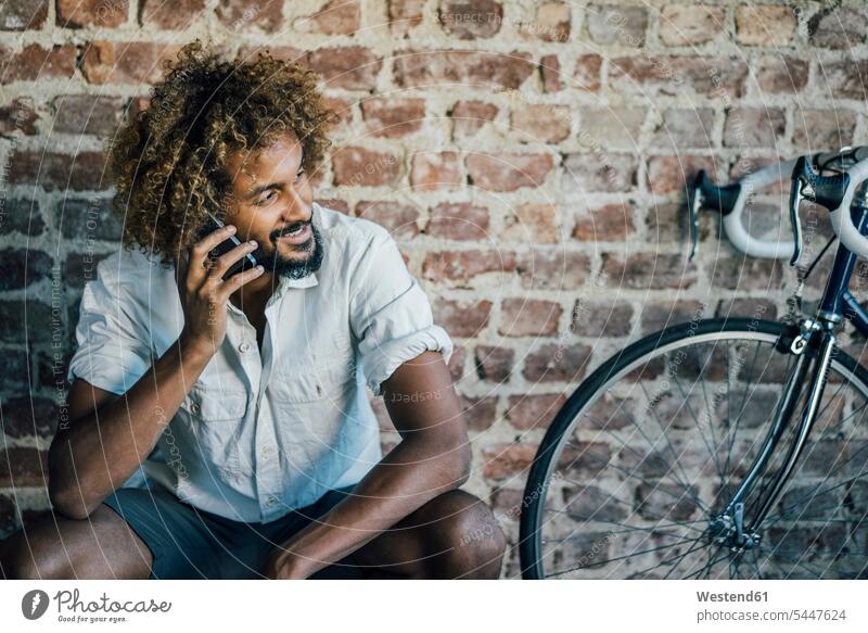 Lächelnder junger Mann mit Fahrrad am Handy lächeln telefonieren anrufen Anruf telephonieren Bikes Fahrräder Räder Rad Mobiltelefon Handies Handys Mobiltelefone