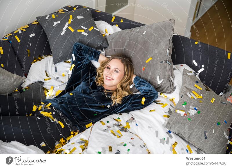 Porträt einer lachenden jungen Frau, die auf einem mit Konfetti bedeckten Bett liegt Betten Confetti zugedeckt abgedeckt verhüllt bedecken weiblich Frauen