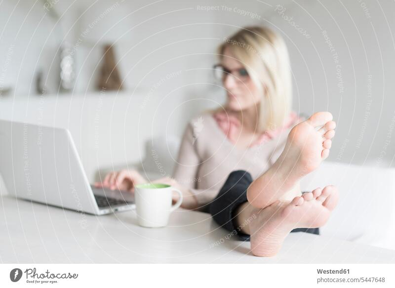 Frau sitzt am Tisch mit erhobenen Füßen am Laptop weiblich Frauen Notebook Laptops Notebooks Tische Erwachsener erwachsen Mensch Menschen Leute People Personen