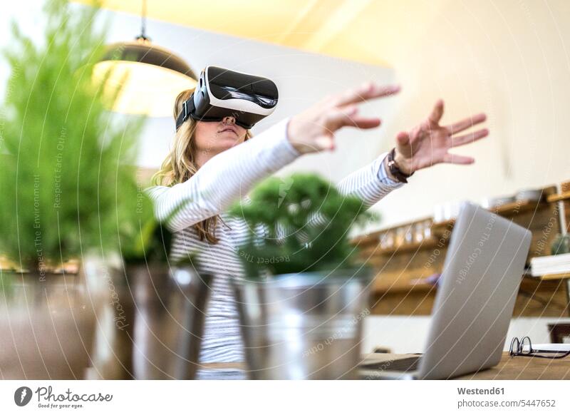 Frau mit VR-Brille und Laptop zu Hause Notebook Laptops Notebooks benutzen Tisch Tische Zuhause daheim Virtuelle Realität Virtuelle Realitaet Brillen weiblich