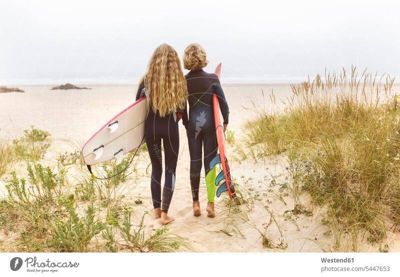 Spanien, Aviles, Rückansicht von zwei jungen Surfern am Strand Beach Straende Strände Beaches Teenager Jugendliche Heranwachsende Pubertierende Wellenreiter