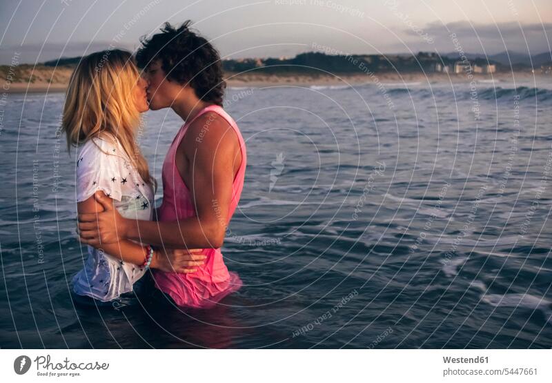 Junges Paar küsst sich in der Abenddämmerung im Meer Meere küssen Küsse Kuss Pärchen Paare Partnerschaft Gewässer Wasser Mensch Menschen Leute People Personen