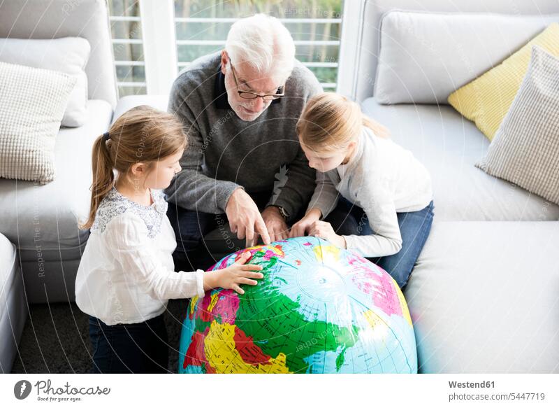 Zwei Mädchen und Großvater mit Globus im Wohnzimmer Wohnraum Wohnung Wohnen Wohnräume Wohnungen weiblich Opa Großpapa Großpapas Opas Opi Großväter Opis