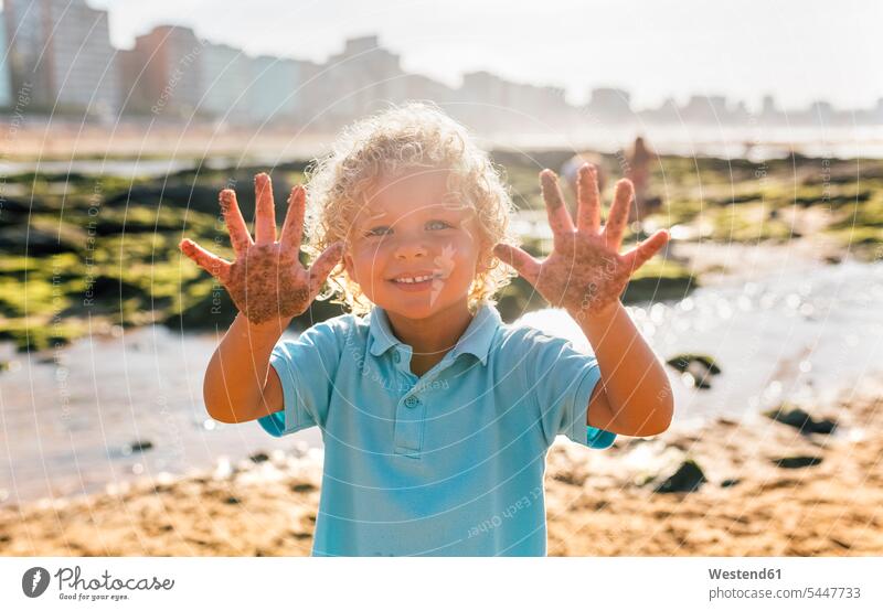Porträt eines lächelnden kleinen Jungen, der seine sandigen Hände am Strand zeigt Portrait Porträts Portraits Buben Knabe Knaben männlich Hand Kind Kinder Kids
